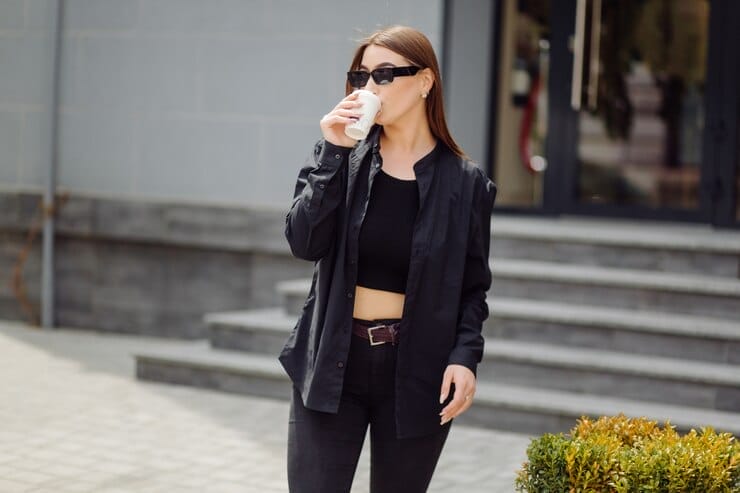 A woman drinking, in black jacket, balck tank  top and a black jean